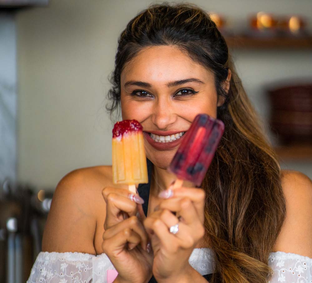 Woman smiling and holding up Mexican Paletas made with Ultima Replenisher Electrolyte Hydration Powder
