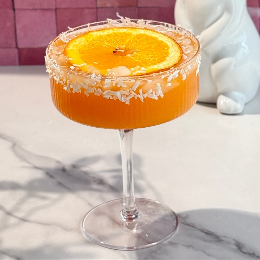 Ultima Citrus Carrot Glow Mocktail image of cocktail orange color with coconut rim and large orange slice.