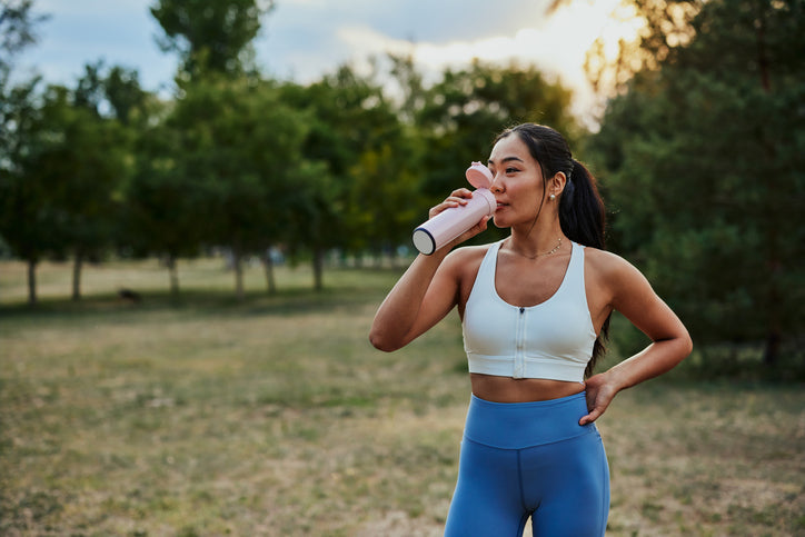woman drinking from water bottle after exercise outdoors