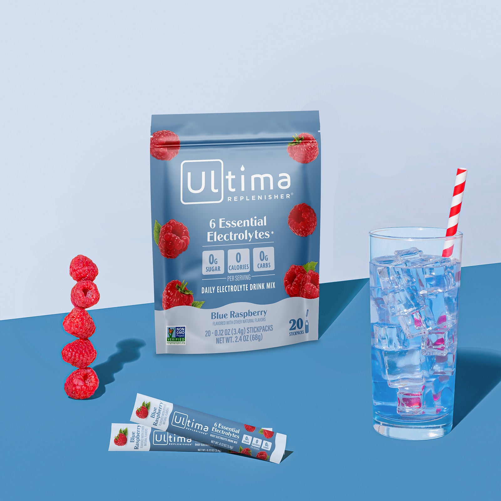 Ultima Replenisher Blue Raspberry electrolyte hydration powder pouch lifestyle with glass and fruit