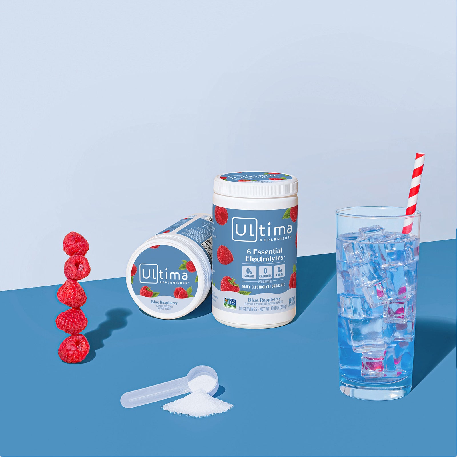 Ultima Replenisher Blue Raspberry electrolyte hydration powder 90 serving canister lifestyle with glass and fruit