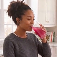Woman drinking a pink smoothie in a kitchen