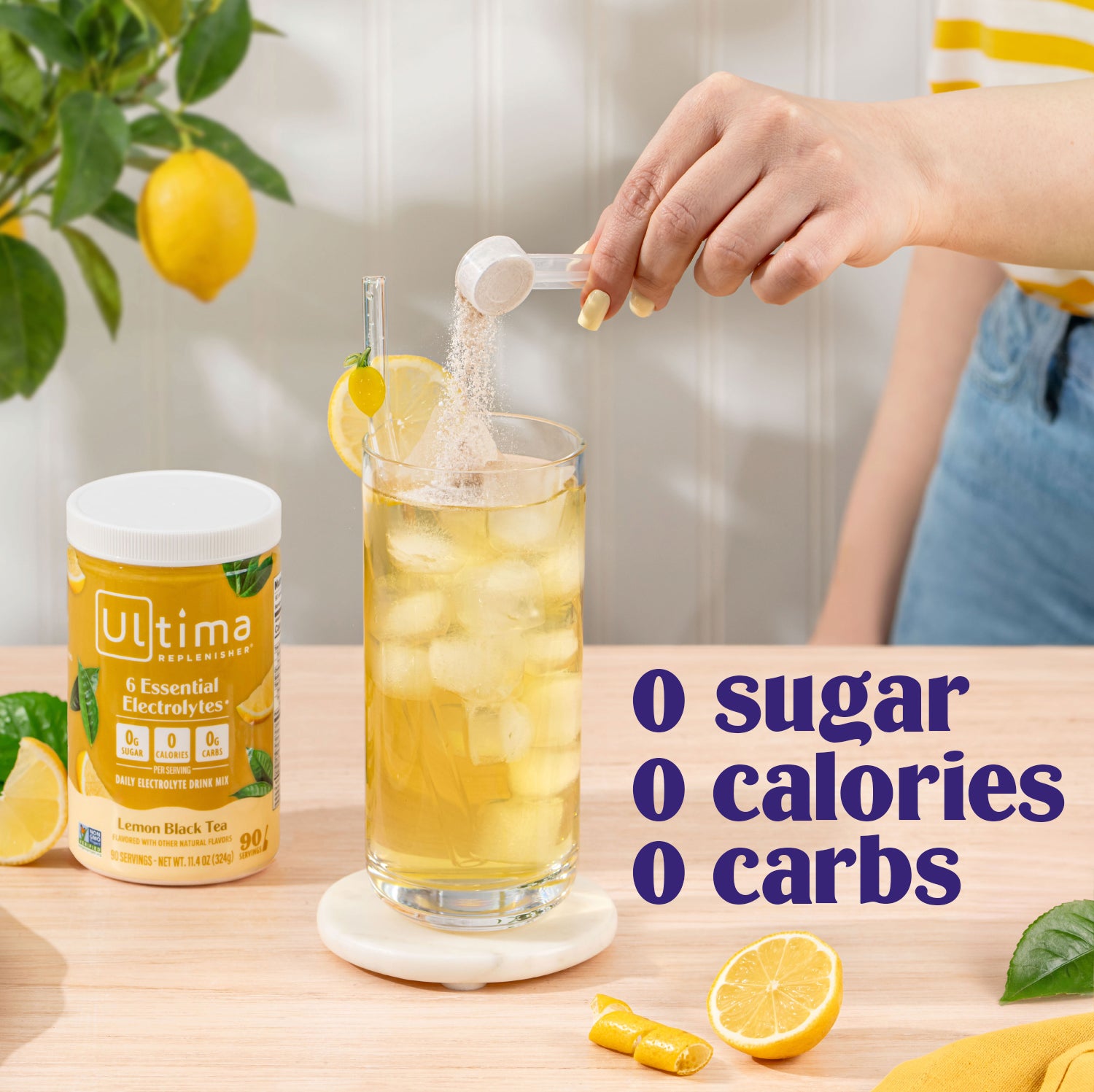 Person pouring a drink into a glass with lemon slices, surrounded by lemons and a 'Ultima' container on a wooden surface.