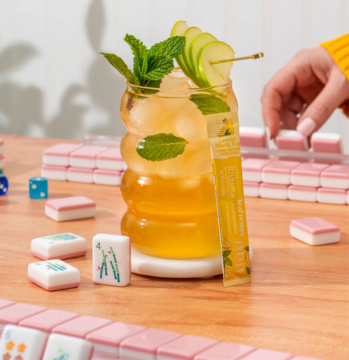 Cocktail with a lemon twist and mint leaf on a table with a mahjong game.