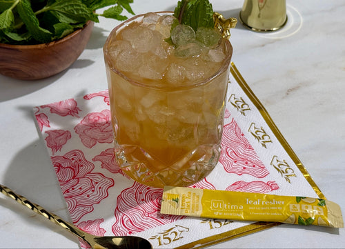 Cocktail with ice and mint leaves on a marble surface with a Rukmini Real Tea bar.