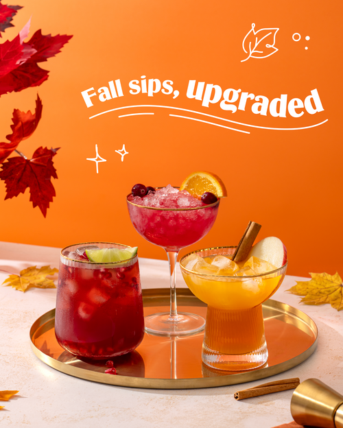 Three colorful fall cocktails on a round gold tray against a bright orange background with white text reading 'Fall sips, upgraded' and autumn leaves around the edges.